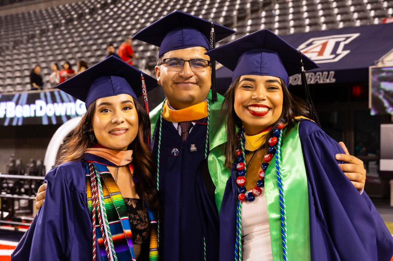 Three graduate students dressed in commencement regalia